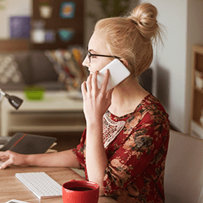 Girl with blonde hair talking on phone with a coffee cup on desk
