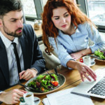 Two business professionals at a lunch meeting reviewing something over their laptop