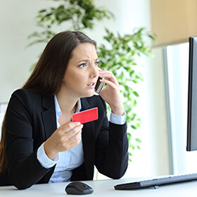 Woman angrily on phone holding credit card and looking at desktop