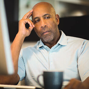 Man sitting at desktop computer with hand on head and coffee mug