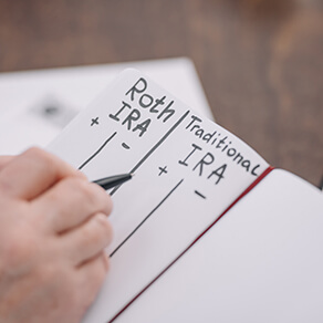 cropped view of senior hand writing in notebook with roth ira and traditional ira words