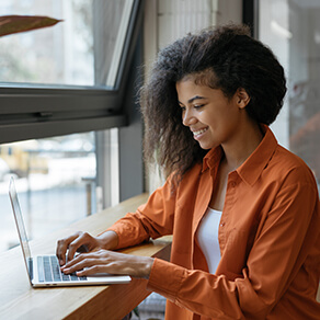 African American woman sitting at desk in front of a window working on independent contractor project