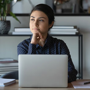 Female sitting at a desk with a laptop and papers looking off into the distance