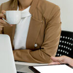 Women holding a coffee cup sitting in front of a laptop