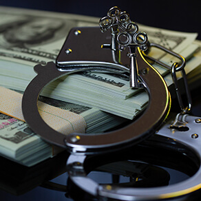 Handcuffs laying on top of stacks of cash in the darkness.