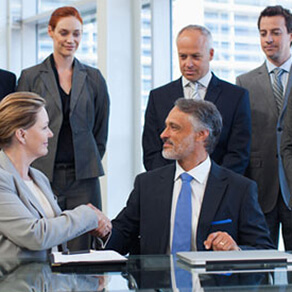 Professional man and woman shaking hands at a business meeting with others looking on