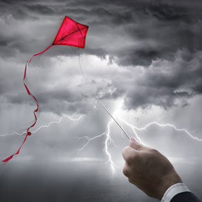 A red kite flying in a lightening storm with a hand reaching up to the storm holding the kite string