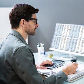 Man sitting at desk looking at computer monitor and taking notes