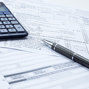 Tax forms in a pile with a pen and a calculator resting on top