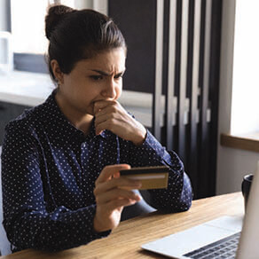 Woman with concerned look looking at her laptop holding her credit card