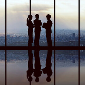Silhouette of three business professionals standing in front of a window