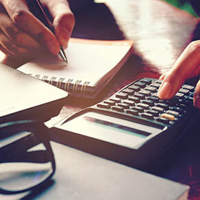 Close up woman hand using calculator and writing make note with calculate about cost at home office.