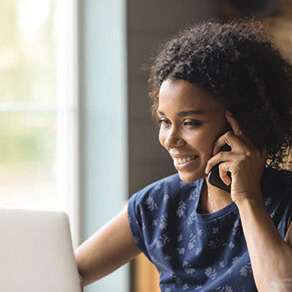 Women on the phone looking at a laptop in front of a window