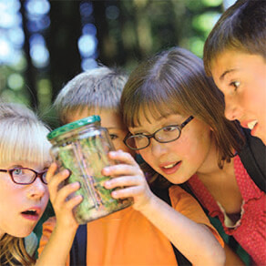 Group of children outdoors looking in awe at contents of a jar
