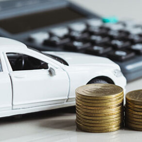 Stack of gold coins next to a model white car and a calculator