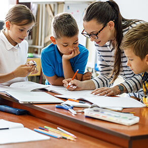 Teacher surrounded by students doing work on desk
