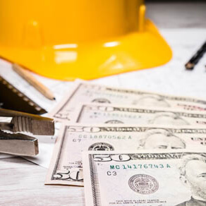 Fifty dollar bills laying next to a yellow hard hat on a desk of paperwork