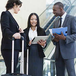 Three business travelers standing in front of an escalator looking at documents