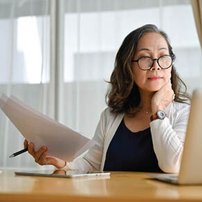 Woman looking at her laptop computer holding a stack of papers