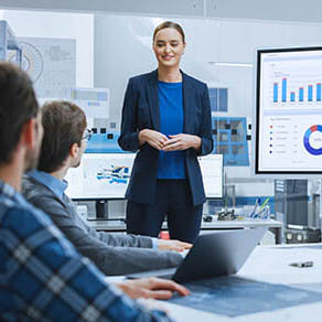 Modern Industrial Factory Meeting: Confident Female Engineer Uses Interactive Whiteboard, Makes Report to a Group of Engineers, Managers Talks and Shows Statistics, Growth and Analysis Information
