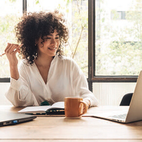 Woman sitting at a desk with a cup of coffee in front of a laptop