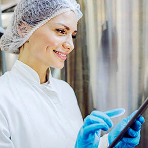 A female diary factory supervisor smiling at the tablet and scrolling on it.