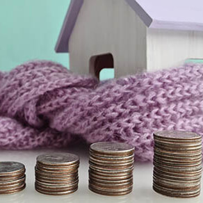 Wooden toy house wrapped in a scarf with stacks of coins next to it