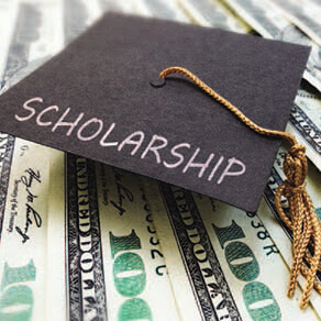 Graduation cap with the word "Scholarship" written on it sitting on top of $100 bills