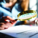 Woman's hand inspecting document with a magnifying glass