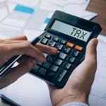 Hand typing the word "TAX" into a calculator