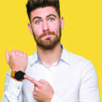 Young man pointing to his watch with disappointment