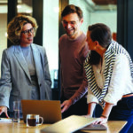 Group of coworkers smiling, in conversation and looking over documents