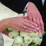 Man and woman's hands showing wedding rings on top of white roses