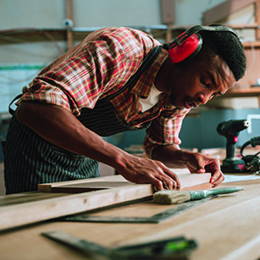 Man, wearing noise cancelling headphones, working on a project at wood working bench