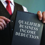 Close up of man in a suit pointing to a book reading, "Qualified Business Inclome Deduction" on the cover