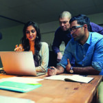 Three coworkers looking over a laptop at a table