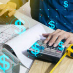 Person working at a desk typing on a calculator with dollar signs over the image