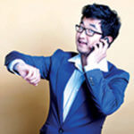 Man holding a cell phone, dressed in a blue suit holding his arm up where his watch is