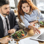 Two business professionals at a lunch meeting reviewing something over their laptop