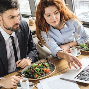 Two business professionals at a lunch meeting reviewing something over their laptop