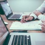 two men looking at documents while sitting at laptops
