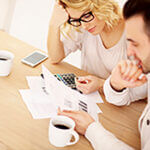 A woman and man reviewing papers, coffee cup, calculator and cell phone on top of a table