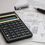 Black hand calculator, pen and pen cap on paper with numeric amounts