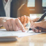 Close up of business man pointing and another person signing estate documents