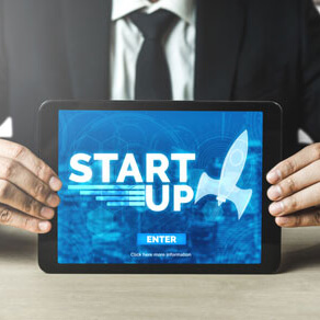 Close up of man in suit holding a tablet computer with a graphic on the screen that reads start up