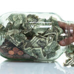 Clear jar stuffed with dollar bills and pennies and hand reaching in to grab some