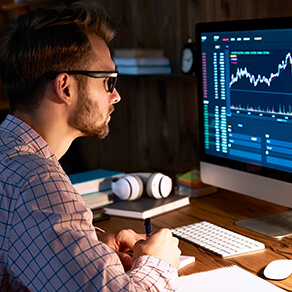 Man sitting in the dark looking at computer monitor with image of graph