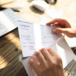 Close-up Of A Businessperson's Hand Opening Envelope With Paycheck Over Wooden Desk