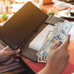 Close up of someone's hands holding money and a restaurant receipt