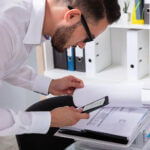 A man looking over documents closely with his phone and taking a photo